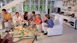 Photo of a group of adults sitting on white sofas in a living room social setting.