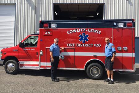 Two first responders standing in front of a fire department ambulance.