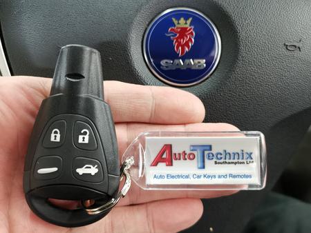Single Saab remote key fob in front of a Saab logo on a Saab steering wheel with a key ring displaying Autotechnix Southampton on it