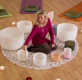 Blond woman sitting on the floor surrounded by singing water bowls creating water sound with a mallet.