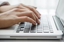 Woman's hands close up shown typing on a laptop keyboard.