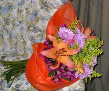 Paper wrapped bouquet with orange lilies, purple alstroemeria and poms, and solidago
