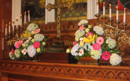 Bookend arrangements on a church altar done in yellow, blue and pink with hydrangea, lilies, gerbera daisies, and roses