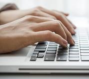 Close-up of woman's hands typing on a laptop keyboard.