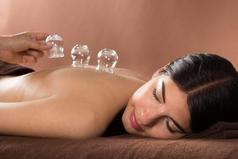 Women with brown hair laying on her left cheek as glass cups are layed on her back by hand represents cupping technique