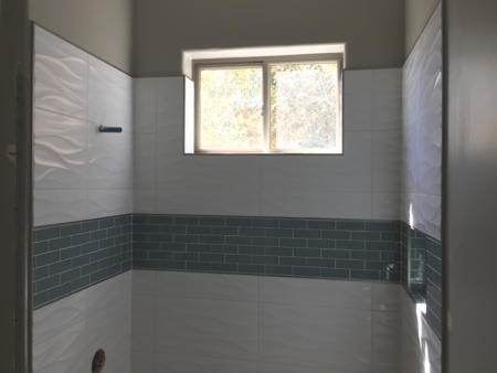 Bathroom with tiled walls above tub with a blue tiled band waist high. And a sliding window above the shower.