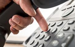 Close up of a hand holding a phone receiver and pushing numbers with index finger.