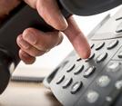 Close up of a hand holding a phone receiver and pushing numbers with index finger.