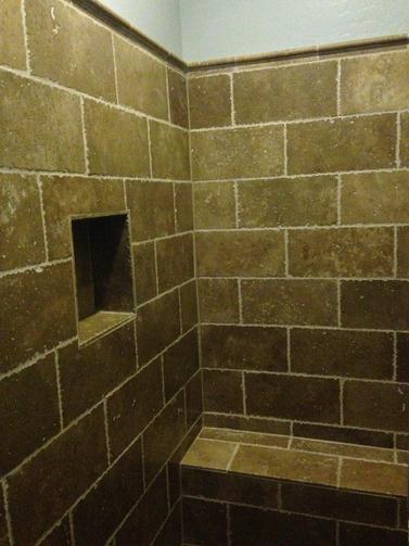 Image of a tiled walk-in shower. with a built in Niche and bench. The tile is a tan, travertine looking tile