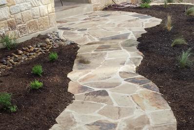 a beautiful custom San Antonio Landscape Design flagstone mortor walkway with deep black mulched beds on both sides and small mexican feather grass and shrubs planted on both side of the landscaping job in San Antonio