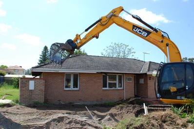 Bulldozer excavator demolishing old residential building on a foggy day-  CanStock