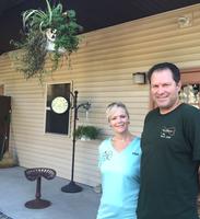 a man wearing a dark shirt and a woman wearing a light blue shirt smile at the camera as they stand at the entrance to the boarding facility