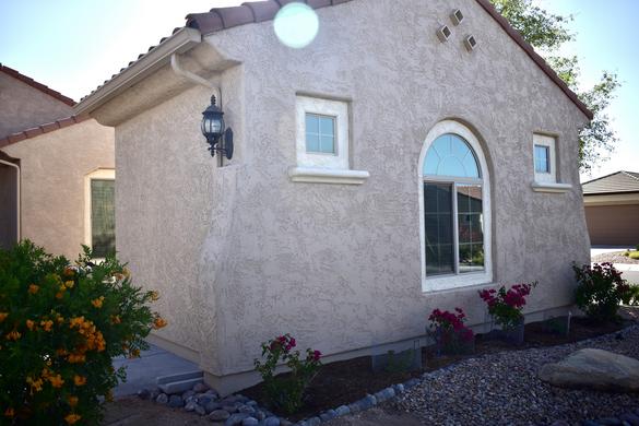 Picture of a newly renovated Garage into a Casita. Casita is newly stuccoed with 3 windows on the front with a light sconce on the side visible. Inside the casita is a room with a full bathroom complete with corner shower, vanity, toilet room, and water heater.