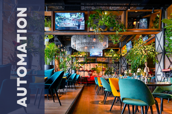 inside of a restaurant with colorful chairs and a big crystal chandelier and a lot of greenery hanging from the ceiling