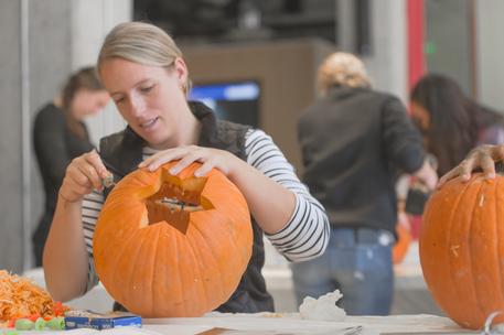 female office worker carving pumpkin with mixed group in backgrounds