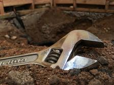 Shiny Wrench in focus resting on the dirt of a torn out shower pan that is being remodeled