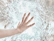 Woman's hand touching a bright clear glass wall that is shattered.