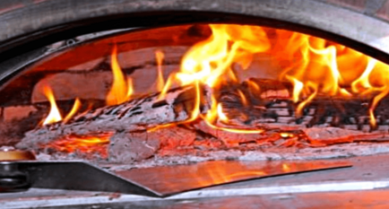 Wood pizza oven having ash shoveled from inside as a fire blazes