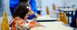 Child writing on a piece of paper sitting at a school desk