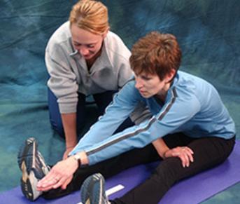 Fitness trainer measuring flexibility levels of the hamstring and back while client is seating down on the floor