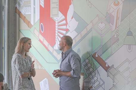 male and female tech employees chatting by mural