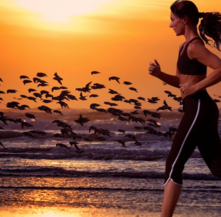 Women running along water with birds in background in sunlight