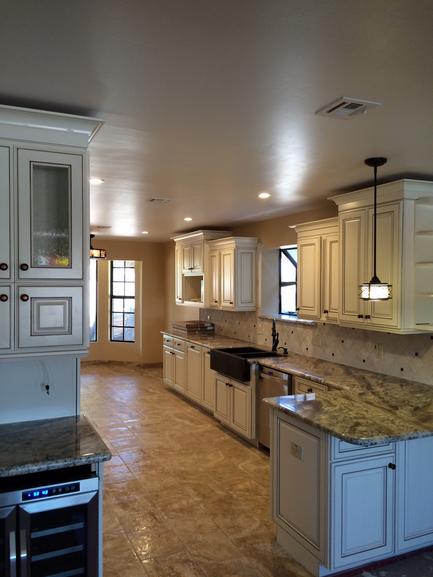 Picture of a remodeled kitchen. Granite counters, new white cabinets with decorate beveled doors. Farmhouse Sink with a window in front of it.