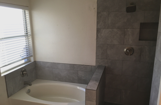 Image of a tiled walk-in shower and a tiled-in tub. Tile is a gray rectangular tile. There is a window on the left above the tub.