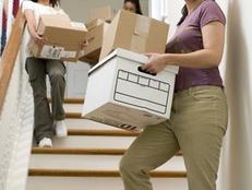 Photograph of woman and her children carrying moving boxes down a staircase in their home.