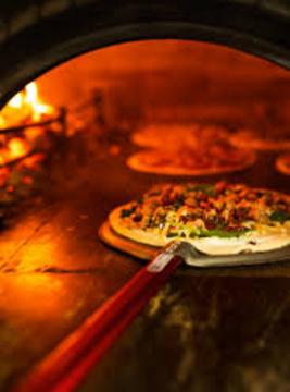 Chef placing an uncooked pizza in a wood burning oven firewood for pizza oven