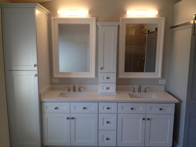 Picture of a newly remodeled bathroom facing the vanity. to the left is a tall linen cabinet. to the right of that is a double sink vanity with a cabinet on the counter separating the two sinks. above the sinks are individual white framed mirrors.