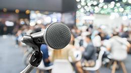 Photo of a microphone with audience members in the background.