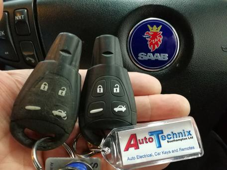 Two Saab remote keys with key ring next to Sabb logo on a steering wheel
