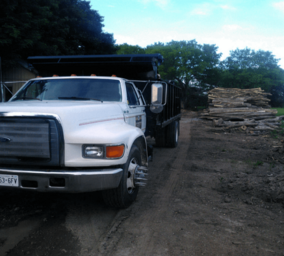 City Loggers delivery truck by stacked firewood logs