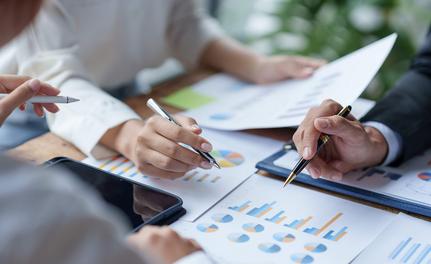 Image of a business table with hands of 3 people reviewing reports