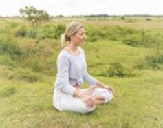 Image of woman sitting cross legged in a green grassy filed connecting to mother earth and reading the land's energy
