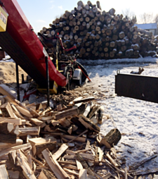 Someone working outside with the firewood conveyor right by a wood pile during the wintertime