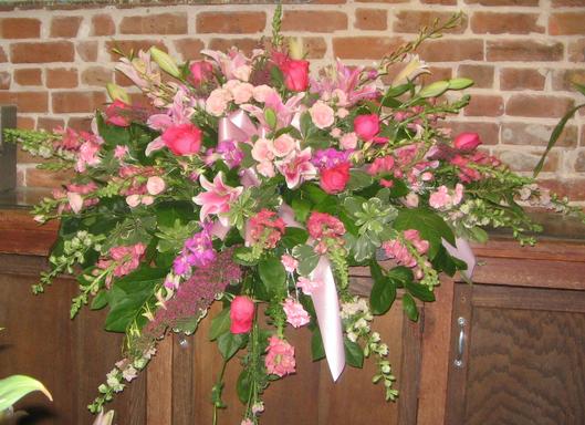 Spray in shades of pink and lavender with roses, stargazers, snapdragons, spray roses, roses, orchids, and a blush ribbon