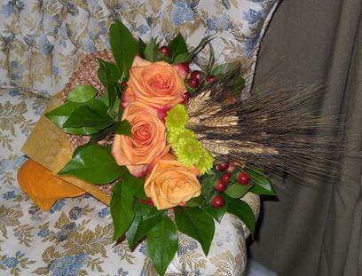 Paper wrapped bouquet with orange roses, red hypericum, green poms, cattails, and salal