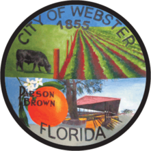 Circular logo for the city of Webster with pastures, a cow, an orange, and a building.