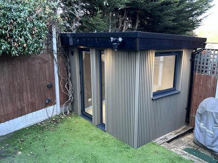 Small walnut colour slatted garden office with dark grey framed glass door and windows