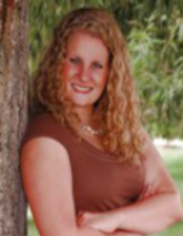 Emily's senior picture, outdoors, leaning against a tree, arms folded, smiling, looking at camera