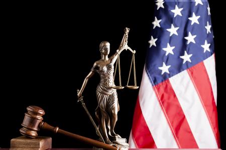Gavel, American flag and a bronze statue of a woman holding up legal scales and a sword