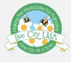 A circular Bee City USA logo with flowers and bees on it, saying "Making The World Safer For Pollinators, One City At A Time."