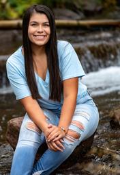 Outdoor picture of Cierra, smiling, looking at the camera, sitting with her hands on her left knee