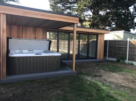 Modern cedar clad garden room with 5 panel bifold doors and a hot tub under a canopy