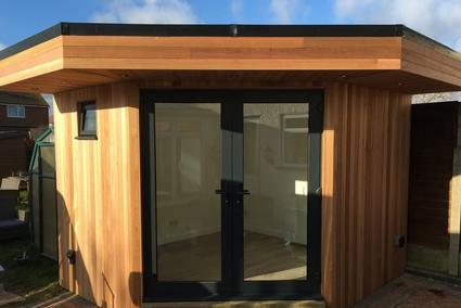 Small hexagon shaped cedar clad garden office with French doors and small window
