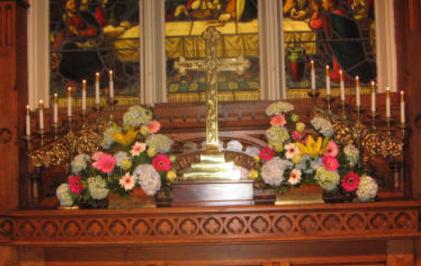 Bookend arrangements on a church altar done in yellow, blue and pink with hydrangea, lilies, gerbera daisies, and roses