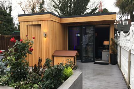 Modern cedar clad garden room with 3 panel bifold doors and an integral shed with a kennel next to it.