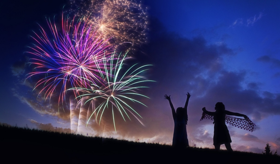 fireworks at evening, with two girls silhouetted celebrating on a hill